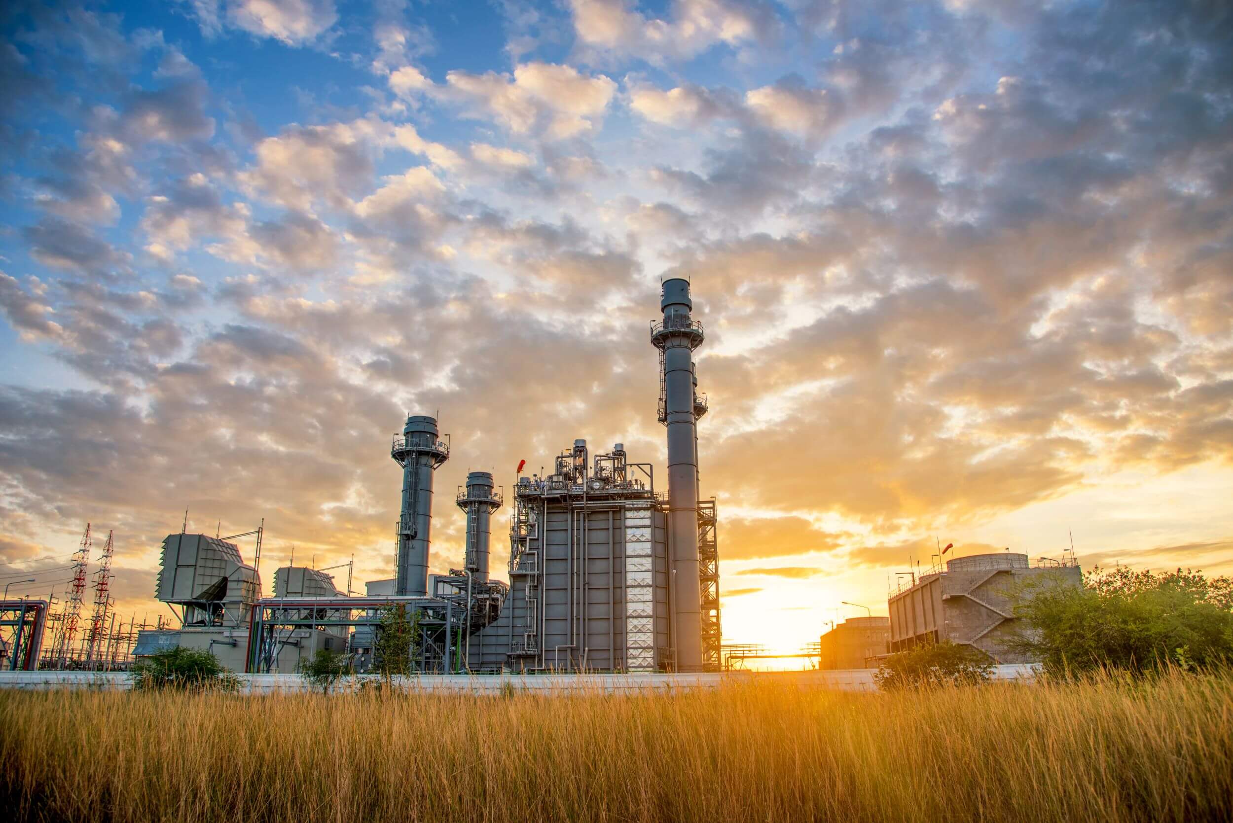 A power generation facility with combustion turbines silhouetted against a dramatic sunset sky, showcasing energy infrastructure and industrial efficiency.