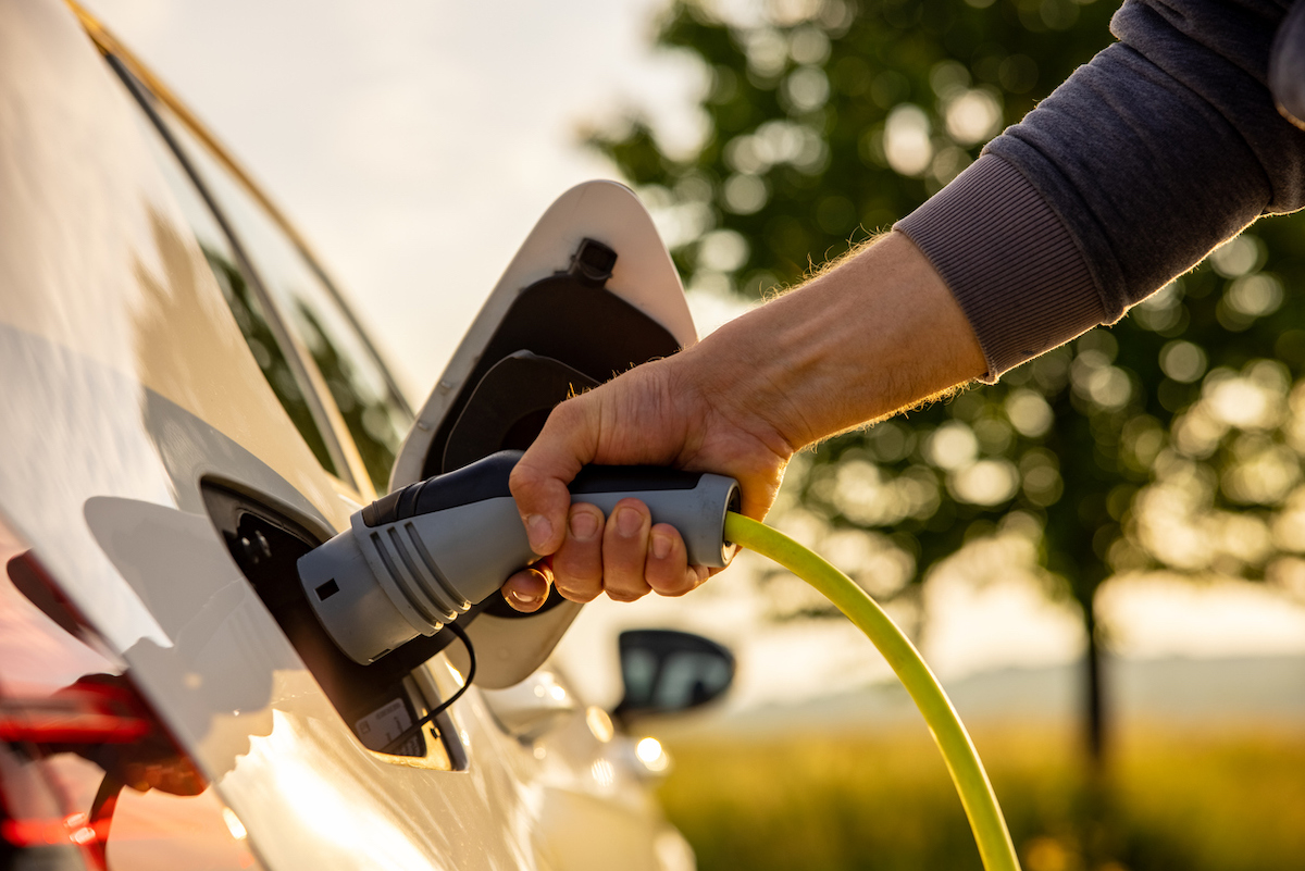 A person charging an electric vehicle at sunrise or sunset